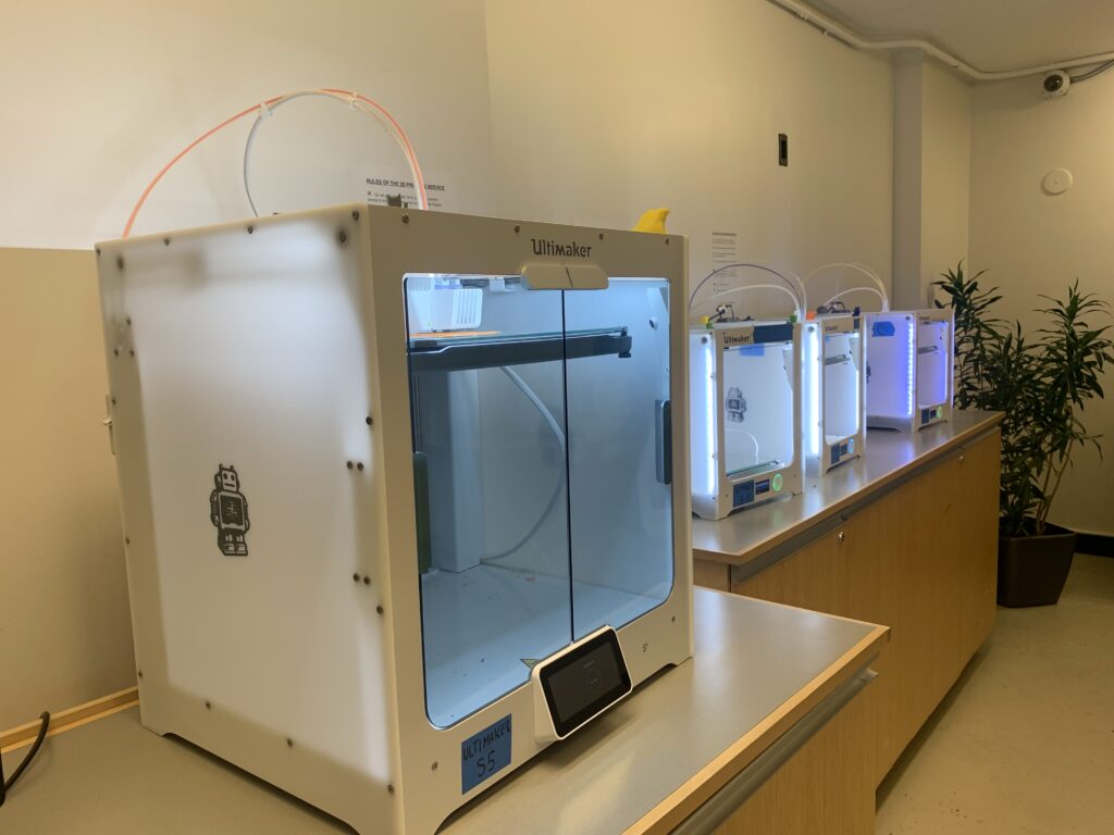 Four 3D printers lined up on cabinets