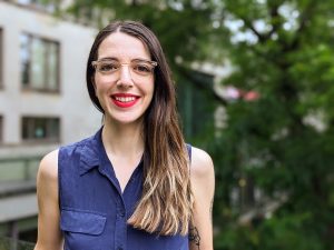 Veronica Bergsten is a young woman with long dark brown hair and glasses. She is smiling widely with bright red lipstick. She is seen from the chest up, wearing a dark blue shirt. 